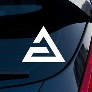 Può includere: Adesivo triangolare geometrico bianco applicato sul lunotto posteriore di un veicolo. L'adesivo presenta un design stilizzato con una forma triangolare e una linea orizzontale nella parte inferiore.