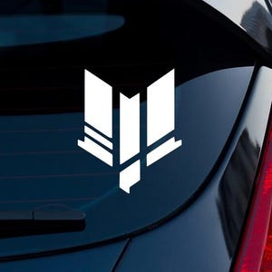 May include: A white vinyl decal featuring a stylized geometric emblem with sharp, angular lines and a symmetrical design. The graphic consists of three vertical segments with a pointed base, applied to the dark glass surface of a vehicle window.