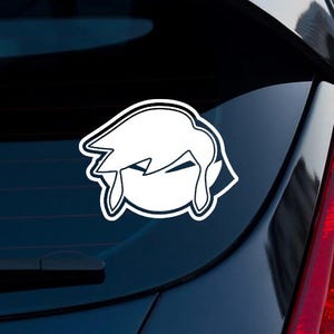 May include: A white vinyl decal featuring a stylized, minimalist silhouette of a character with pointed ears and swept hair, outlined in a thin black border, applied to the dark glass surface of a vehicle rear window.