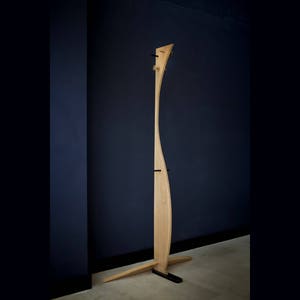 Op de afbeelding: Een hoge, houten kapstok met een gebogen ontwerp. De kapstok heeft een donkerhouten basis en staat op een lichte houten vloer.