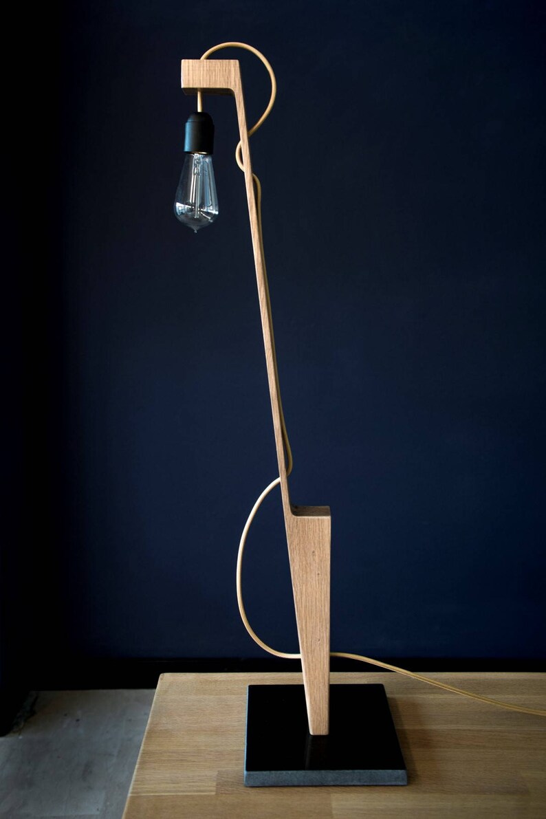 Op de afbeelding: Een houten vloerlamp met een zwart snoer en een gloeilamp. De lamp heeft een eenvoudig, modern ontwerp en is gemaakt van natuurlijk hout.