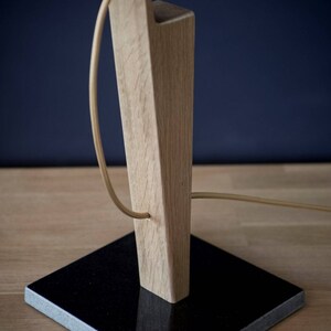 Op de afbeelding: Een houten tafellamp met een zwarte granieten basis. De lamp heeft een snoer dat om de houten basis wikkelt.