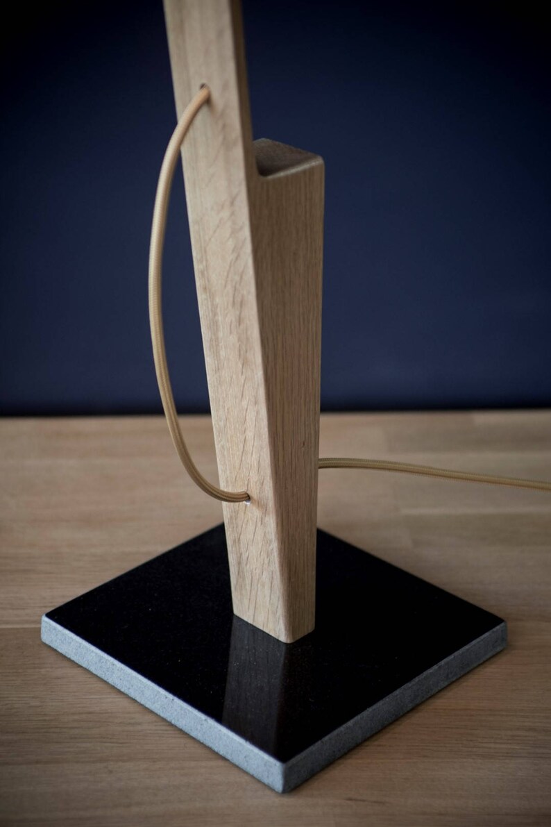 Op de afbeelding: Een houten tafellamp met een zwarte granieten basis. De lamp heeft een snoer dat om de houten basis wikkelt.