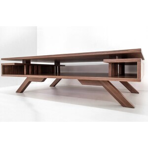 Op de afbeelding: Een moderne salontafel van walnoot hout met een uniek ontwerp met een lager plank en schuine poten.