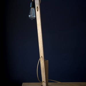 Op de afbeelding: Een houten vloerlamp met een zwarte voet en een heldere glazen lamp. De lamp staat op een houten tafel.