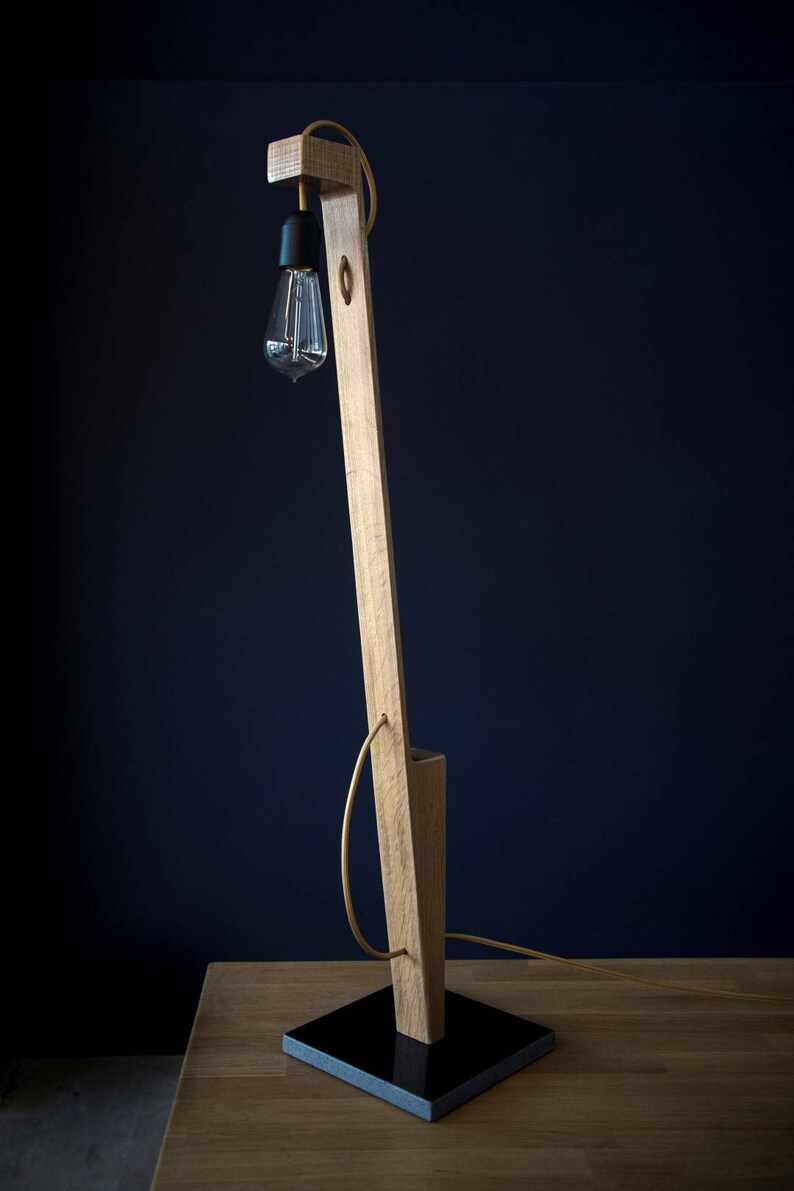 Op de afbeelding: Een houten vloerlamp met een zwarte voet en een heldere glazen lamp. De lamp staat op een houten tafel.