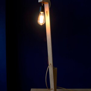 Op de afbeelding: Een houten vloerlamp met een zwarte voet en een gloeilamp. De lamp staat op een houten tafel.