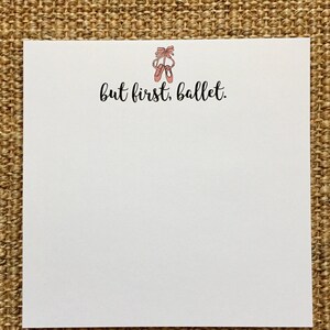 May include: White notepad with the text "but first, ballet." and a drawing of pink ballet shoes with a bow on top.