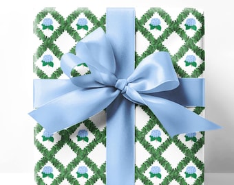 May include: A wrapped gift with a white background. The wrapping paper has a green and white diamond pattern with blue floral accents. A light blue satin ribbon is tied in a bow around the gift.