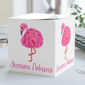 May include: White cube-shaped notepad with a pink flamingo illustration on each side. The notepad has the name "Jessica Adams" printed on the front.