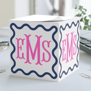 May include: White cube-shaped notepad holder with a blue and white wavy border and the monogram "EMS" in pink letters.