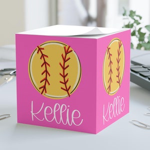 May include: Pink notepad with a yellow softball graphic and the name "Kellie" printed on it.