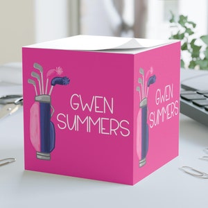 May include: Pink desk notepad with a golf bag and clubs design. The notepad has the name "GWEN SUMMERS" printed on it.