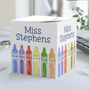 May include: White cube-shaped desk organizer with a colorful crayon design and the name "Miss Stephens" on two sides.