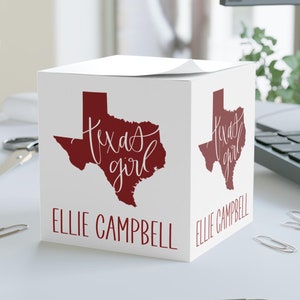 May include: White cube-shaped notepad with a red outline of the state of Texas and the text "Texas girl" in white script. The name "Ellie Campbell" is printed on the bottom of the cube.