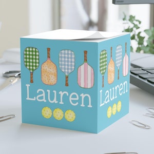 May include: A blue notepad with a personalized name "Lauren" and a design of colorful paddleball rackets and yellow balls.