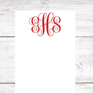 May include: A white notepad with a red monogram of the letters "JHS" in a cursive font.