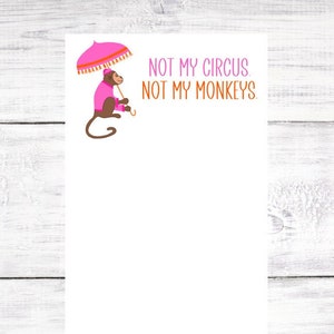 May include: A white notepad with a pink monkey holding a pink and orange umbrella. The notepad has the text "NOT MY CIRCUS NOT MY MONKEYS." printed on it.