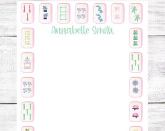 May include: A white notepad with a pink border features a design of mahjong tiles with various symbols and images. The name "Annabelle Smith" is printed at the top of the notepad.