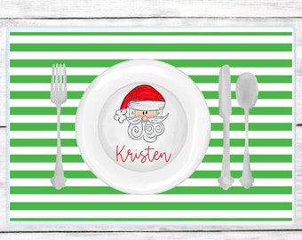 May include: Green and white striped placemat with a white plate featuring a cartoon Santa Claus and the name "Kristen" in red.