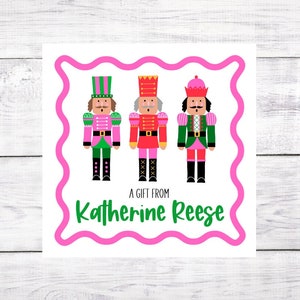 May include: Three nutcracker figurines with pink and green accents. The nutcrackers are standing in a row. The text "A gift from Katherine Reese" is below the nutcrackers.