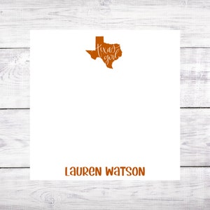 May include: A white card with an orange outline of the state of Texas and the text "Texas girl" in white script. The name "LAUREN WATSON" is printed in orange at the bottom of the card.