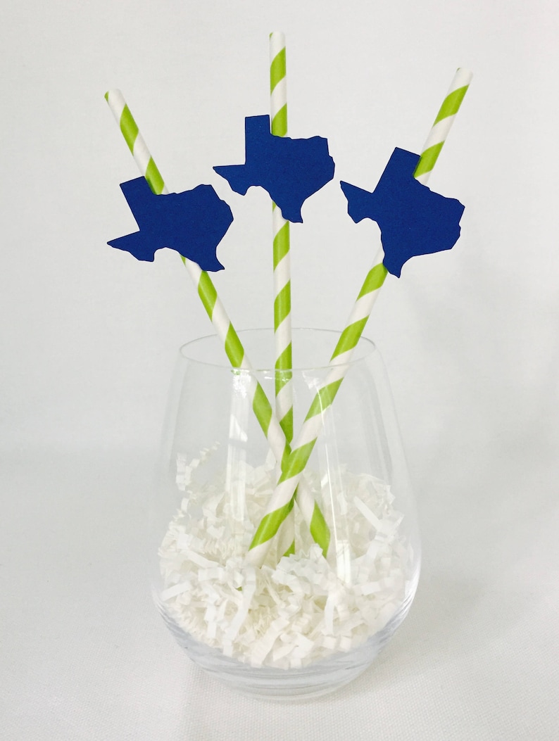 Pode incluir: Um copo transparente cheio de peda&ccedil;os de papel branco cont&eacute;m tr&ecirc;s canudos. Cada canudo tem um padr&atilde;o listrado verde e branco e um recorte azul em forma de Texas. Os canudos s&atilde;o um elemento decorativo.