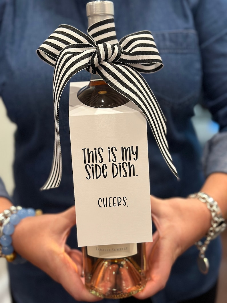 May include: A white wine bottle gift tag with black and white striped ribbon. The tag reads "This is my side dish. Cheers."