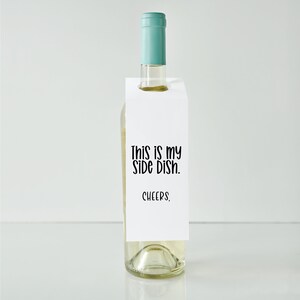 May include: White wine bottle with a white paper gift tag that says "This is my side dish. Cheers."
