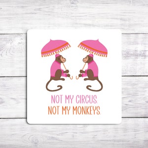 May include: White coaster with two pink umbrellas and two monkeys wearing pink jackets. The text "Not my circus. Not my monkeys." is printed below the monkeys.