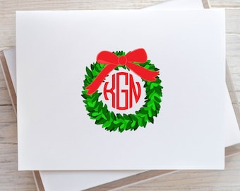 May include: A white card with a green wreath with a red bow and a monogram that says "KGN".