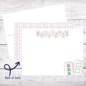 May include: A white card with a pink and green border featuring a row of pink mahjong tiles with various symbols and numbers. The back of the card has a pink and green pattern.