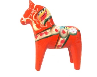 May include: A traditional Swedish Dala horse figurine, hand-painted in bright red with intricate details in yellow, green, and blue. The horse has a white bridle and a saddle with floral patterns.