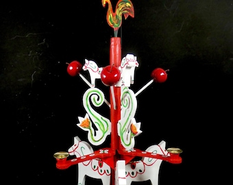May include: A red and white wooden Christmas tree ornament with a rooster on top and four white horses with green and red details. The ornament has four red apples and four candle holders.