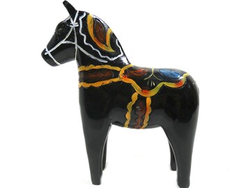 May include: A black wooden Dala horse with yellow, orange, brown, and blue painted details. The horse has a white painted bridle and saddle.