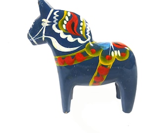 May include: A hand-painted, wooden Dala horse figurine. The horse is dark blue with decorative red, yellow, and white painted details. The horse has a saddle and bridle design. The figurine is a traditional Swedish folk art item.