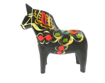 May include: A black wooden horse with colorful painted designs. The horse is a traditional Swedish Dala horse, a popular folk art souvenir.