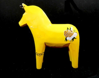 May include: A yellow wooden Dala horse with black painted details, including a rose and a banner with the word "Mamma" on it.