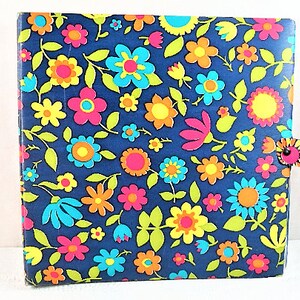Puede incluir: Una carpeta azul con un patrón floral en tonos de rosa, amarillo, naranja y azul. La carpeta tiene una pequeña pestaña naranja y negra en el lado derecho.