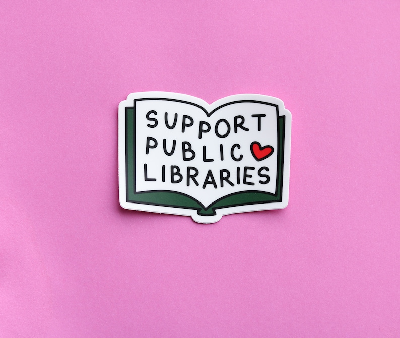 Pode incluir: Um adesivo branco com a forma de um livro verde com o texto "SUPPORT PUBLIC LIBRARIES" e um cora&ccedil;&atilde;o vermelho.