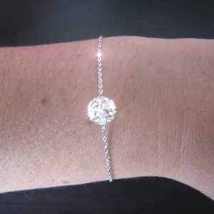 Puede incluir: Un brazalete de cadena de plata con un dije redondo, brillante, incrustado de cristales.
