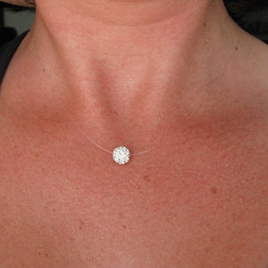 May include: A delicate necklace featuring a square, sparkling pendant composed of numerous small, clear crystals. The pendant is suspended on a nearly invisible, thin, clear cord, creating a floating effect against the skin. The necklace is a piece of jewelry.