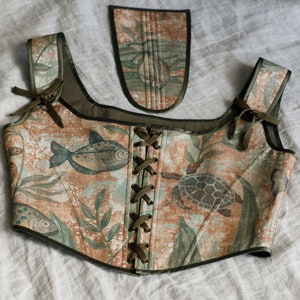 May include: A brown and green corset with a lace-up front and a matching fabric pocket. The corset features a sea-life print with fish, turtles, and seaweed.