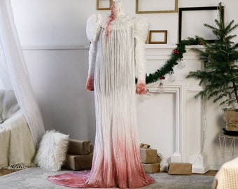 May include: A white gown with a red ombre effect, displayed on a mannequin in a room with a fireplace and a Christmas tree.