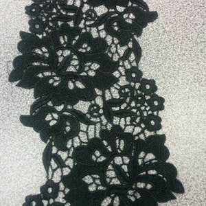 May include: Black lace trim with a floral design. The lace is delicate and intricate, with a repeating pattern of flowers and leaves.
