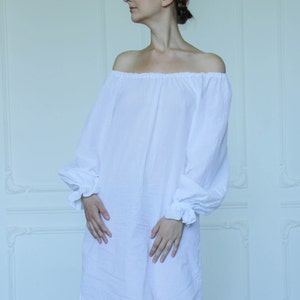 May include: A white off-the-shoulder dress with long sleeves and a gathered neckline. The dress is made of a lightweight fabric and has a relaxed fit.