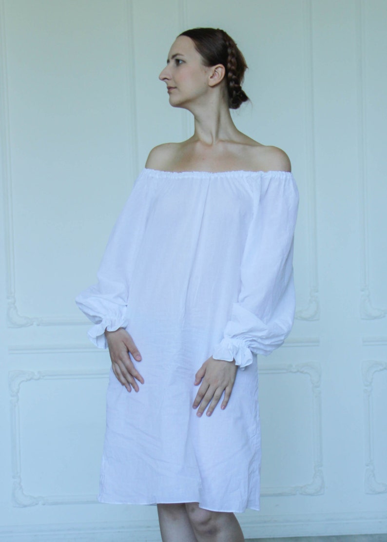May include: A white off-the-shoulder dress with long sleeves and a gathered neckline. The dress is made of a lightweight fabric and has a relaxed fit.