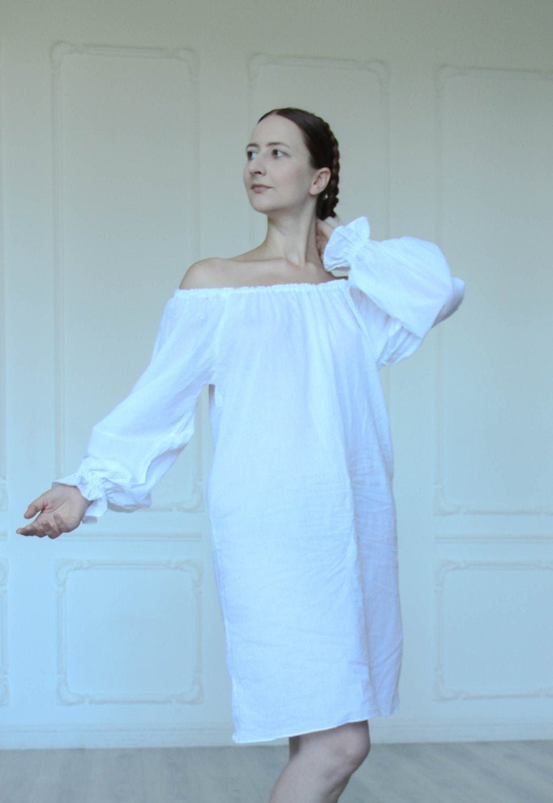 May include: A white off-the-shoulder dress with long, gathered sleeves and a loose, flowing fit.
