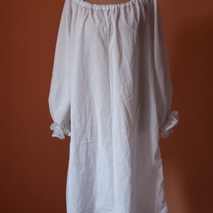 May include: A white cotton chemise with a gathered neckline and long sleeves. The sleeves have ruffles at the cuffs.