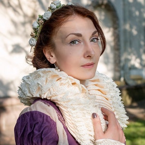 May include: A woman with red hair wearing a purple and gold dress with a white lace collar and a flower crown.